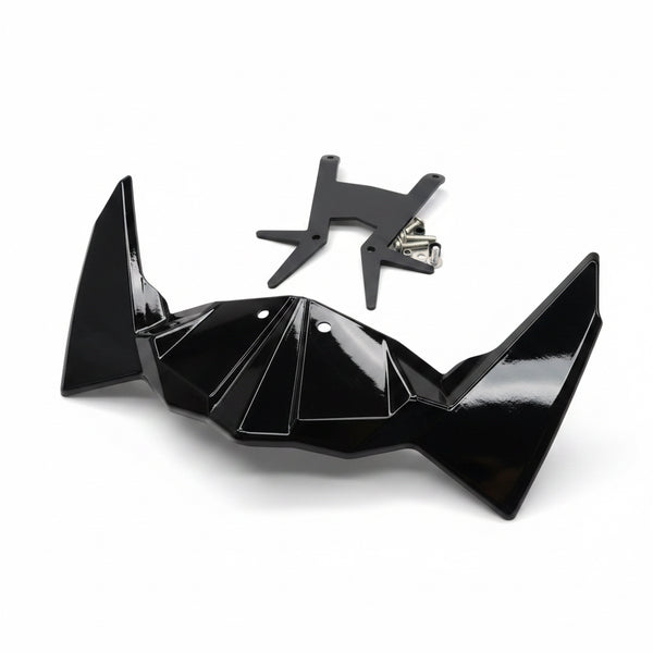 A glossy black bat-wing shaped accessory and a small black metal bracket placed on a light wood tabletop, with a red-handled tool and packaged items partially visible around it.