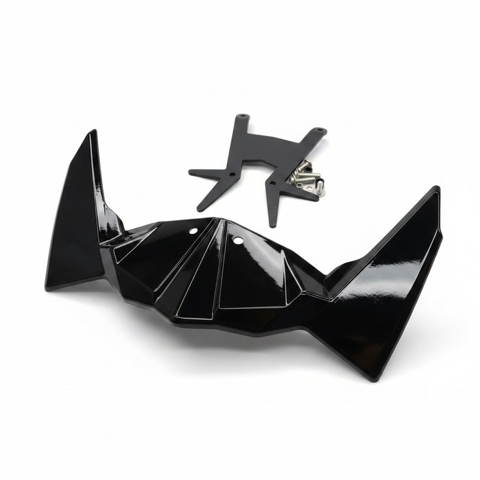 A glossy black bat-wing shaped accessory and a small black metal bracket placed on a light wood tabletop, with a red-handled tool and packaged items partially visible around it.