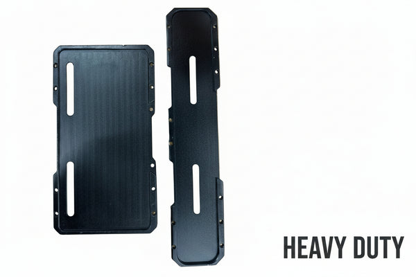Two black rectangular metal mounting plates with elongated cutouts, placed on a textured beige bubble-wrap surface.