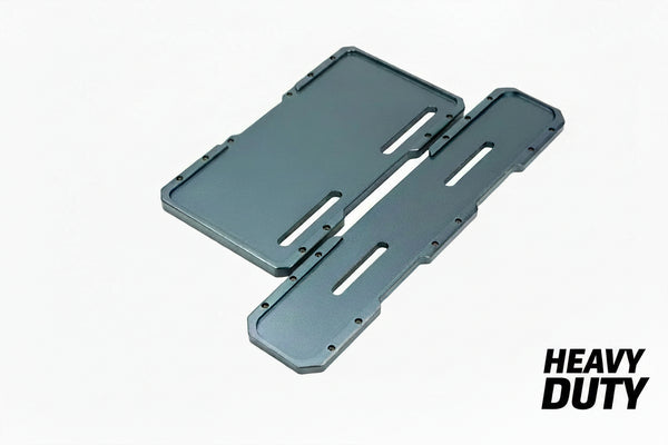 Two dark gray metal mounting brackets with cutout slots, placed on brown bubble wrap packaging.