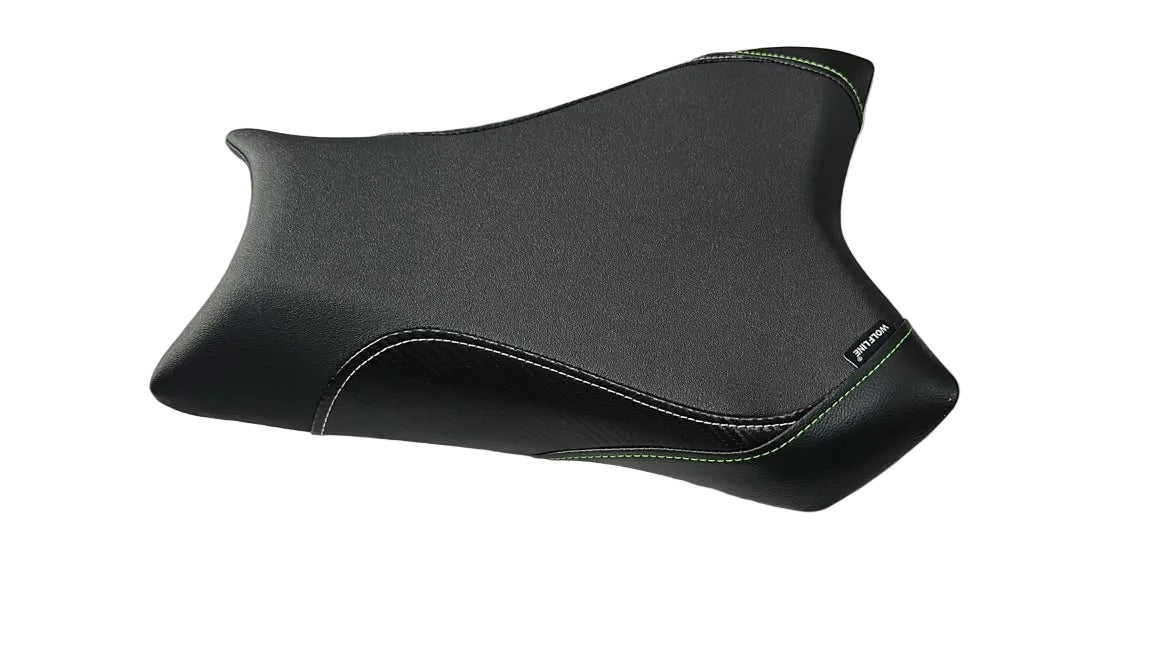 A black motorcycle seat pad with light green contrast stitching, displayed on a white plastic sheet in a warehouse setting.
