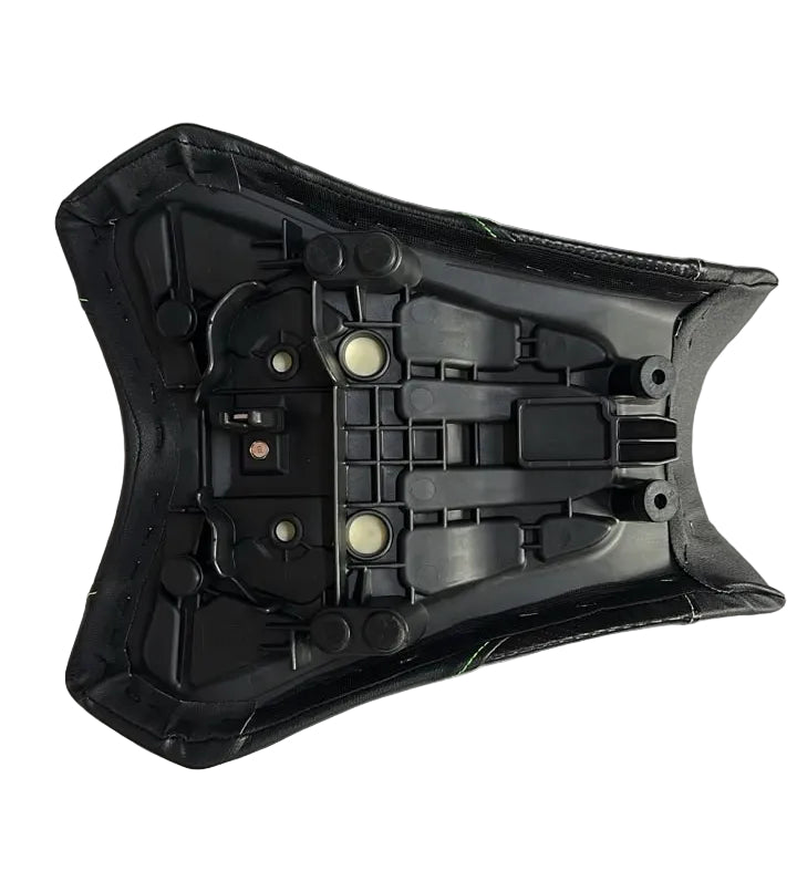 A black plastic motorcycle or scooter seat shell with molded mounting points, photographed from above on a white sheet of paper over a gray floor.
