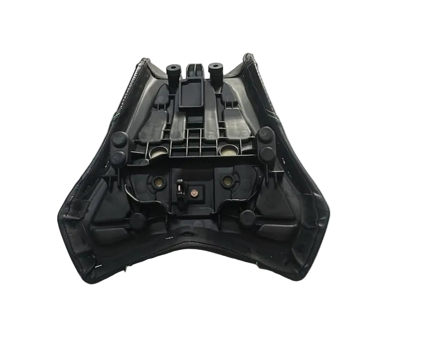 A black plastic motorcycle or scooter seat shell with integrated mounting points, shown from the underside on a white sheet in a warehouse setting.