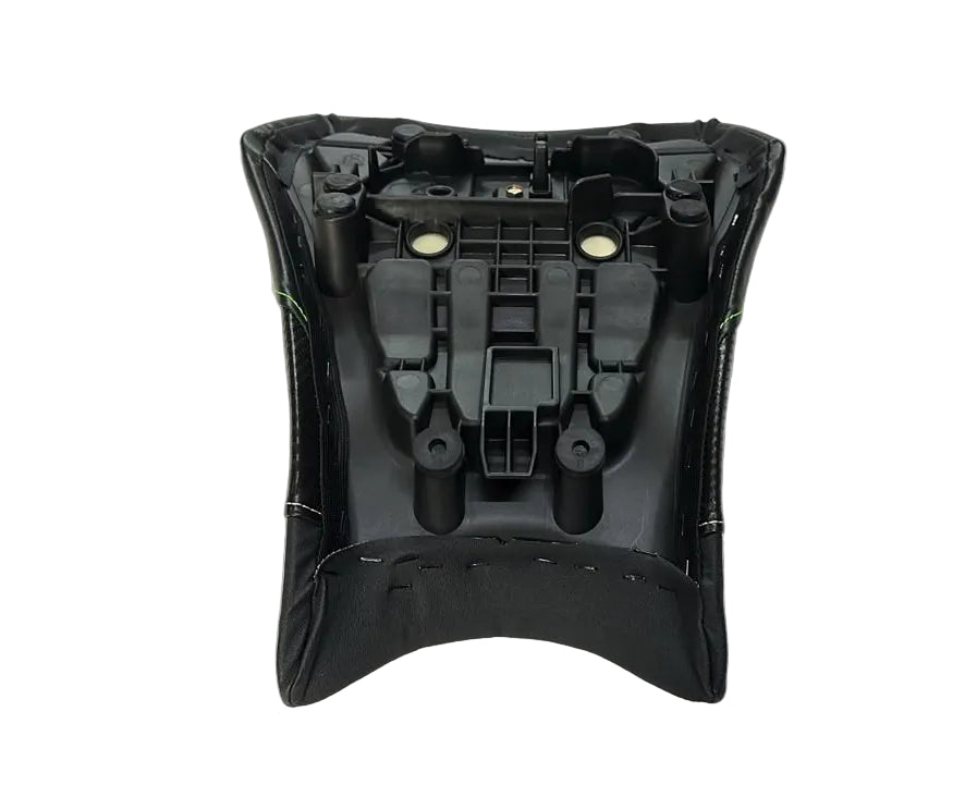 A black plastic automotive seat or console component with molded cavities and small circular openings, photographed from above on a white sheet in a warehouse-like setting.