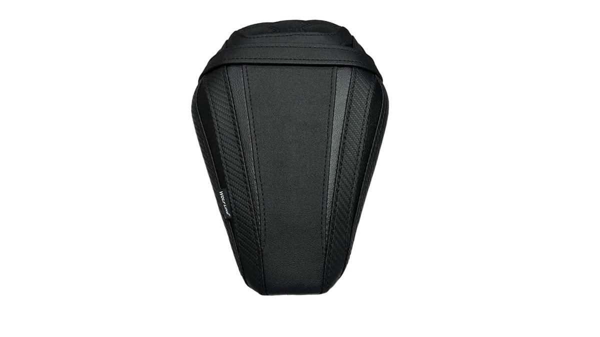 A black motorcycle or scooter seat cover with a textured carbon-fiber pattern, shown on a white protective sheet with cardboard boxes in the background.
