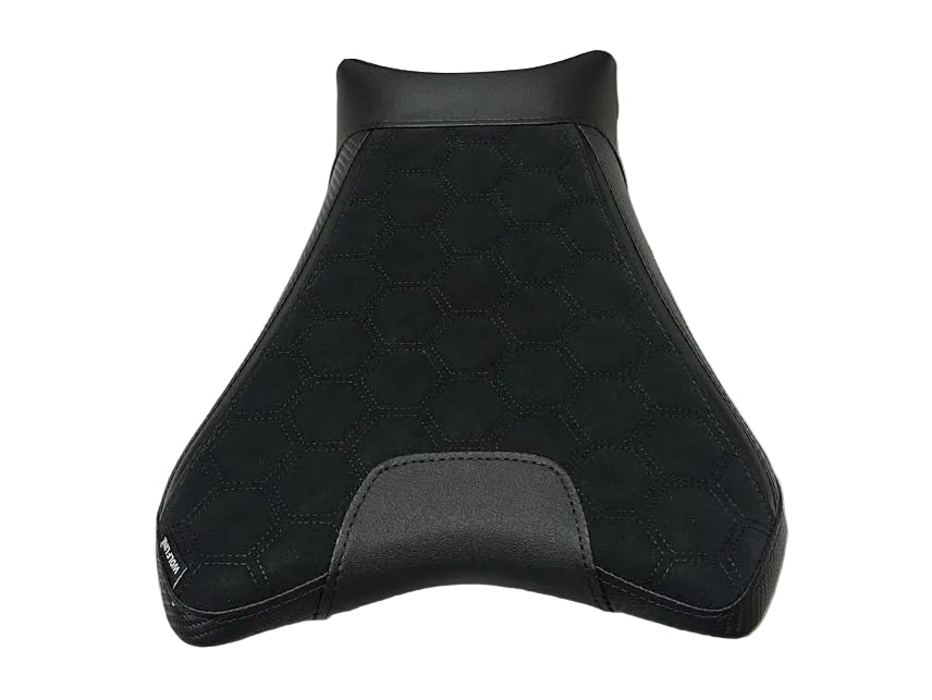 A black motorcycle or scooter seat cover with a textured suede-like upper section and smooth black lower trim, displayed on a white protective sheet in a warehouse setting.