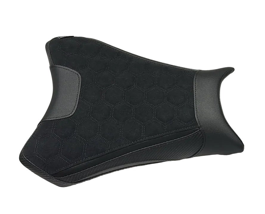 A black motorcycle or scooter seat pad with a textured honeycomb pattern, placed on a white protective sheet in a warehouse setting.