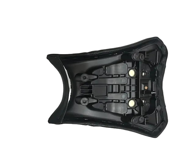 A black plastic motorcycle or scooter seat shell with mounting holes, resting on a white protective sheet on a warehouse floor surrounded by cardboard boxes.