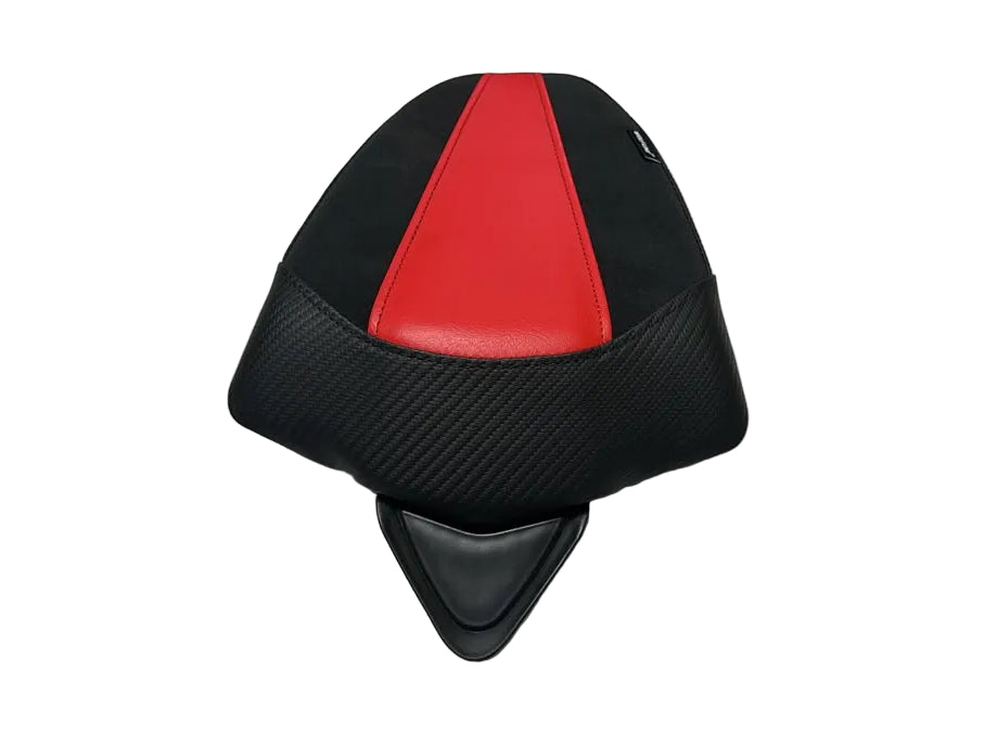 A motorcycle or scooter rear seat pad with a black carbon-fiber textured pattern and a red center stripe, resting on a white sheet in a warehouse-like setting.