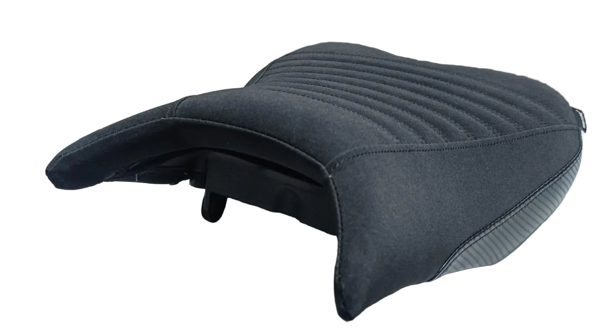 A black motorcycle or scooter seat cover cushion with quilted stitching, shown resting on a white surface in what appears to be a warehouse or storage area.