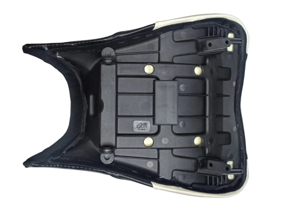A black molded plastic seat shell or backrest component with white trim, photographed from above on a white cloth-covered surface. Parts of people's legs and clothing are visible at the edges, indicating a casual, non-studio setting.