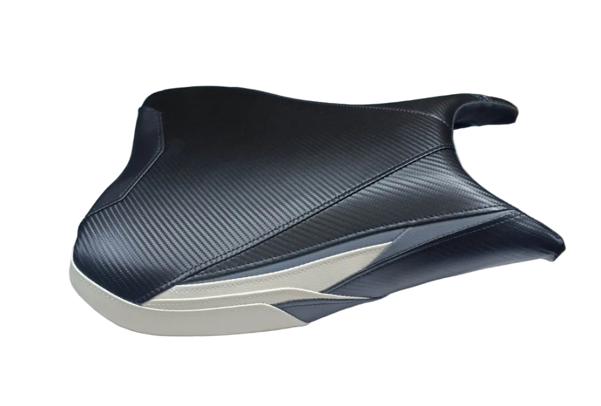 A motorcycle or scooter seat cover with a black carbon-fiber-look pattern and a cream-colored base, displayed on a white sheet with cardboard boxes in the background.