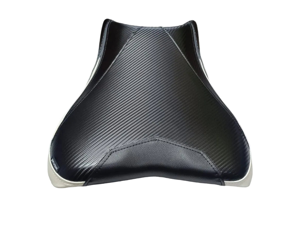 A black carbon-fiber-pattern motorcycle or scooter seat with white trim, resting on a white sheet inside a warehouse or storage area.