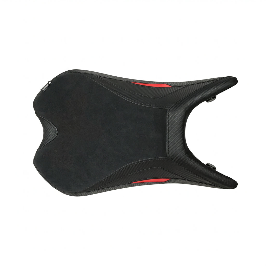 A black motorcycle or scooter seat cover with small red accents, displayed on a white pillow in a warehouse or shipping area with people and cardboard boxes visible around it.