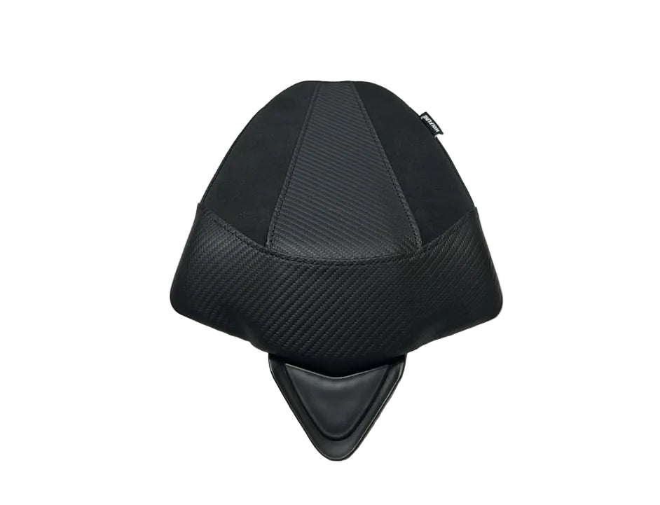 A black motorcycle or scooter seat cover with a carbon fiber pattern, displayed on a white protective sheet in a warehouse setting.