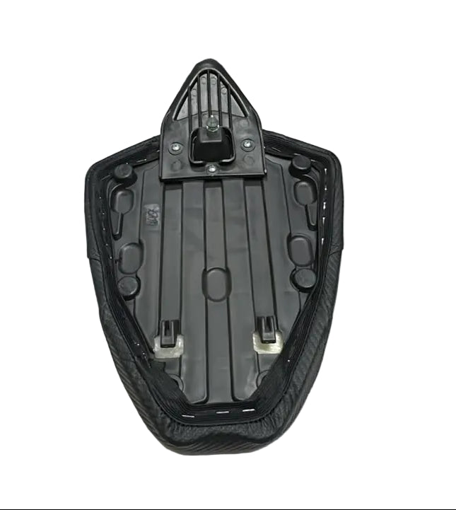 A black motorcycle or scooter seat cushion with a central mounting bracket, displayed on a white sheet in what appears to be a warehouse or storage area with people standing nearby.