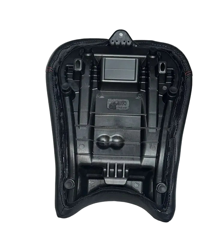 A black motorcycle or bicycle seat cushion cover with an integrated backrest, laid flat on a white fabric-covered surface. A person wearing a plaid shirt is visible at the bottom of the frame.