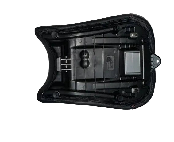A black plastic motorcycle or scooter seat shell with its center console mounted, resting on a white foam sheet on a person's lap in a warehouse or workshop setting.