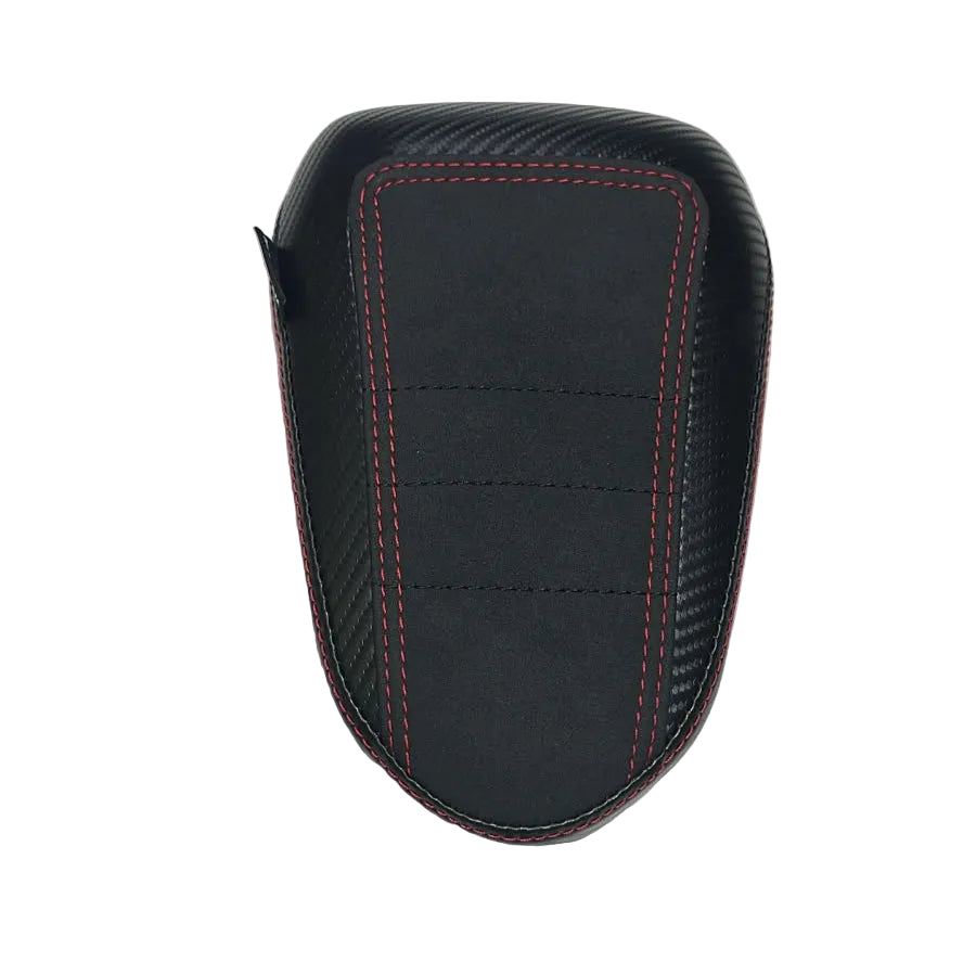 A black motorcycle or scooter seat backrest cover with red contrast stitching and a carbon fiber pattern, placed on a white fabric-covered surface.