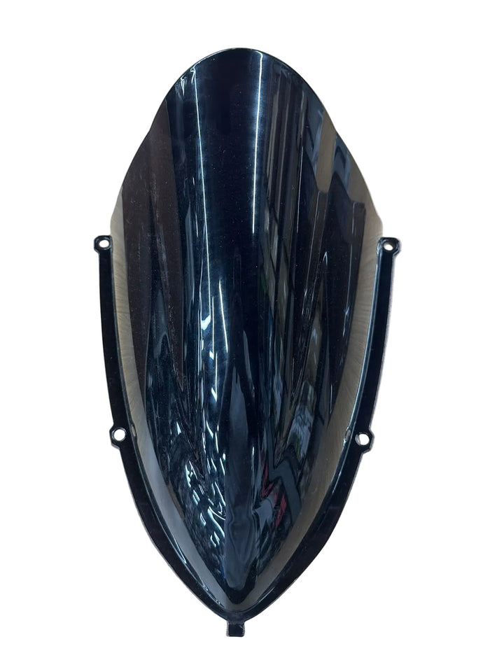 A glossy black motorcycle windshield with mounting brackets, shown on a light wood grain tabletop.
