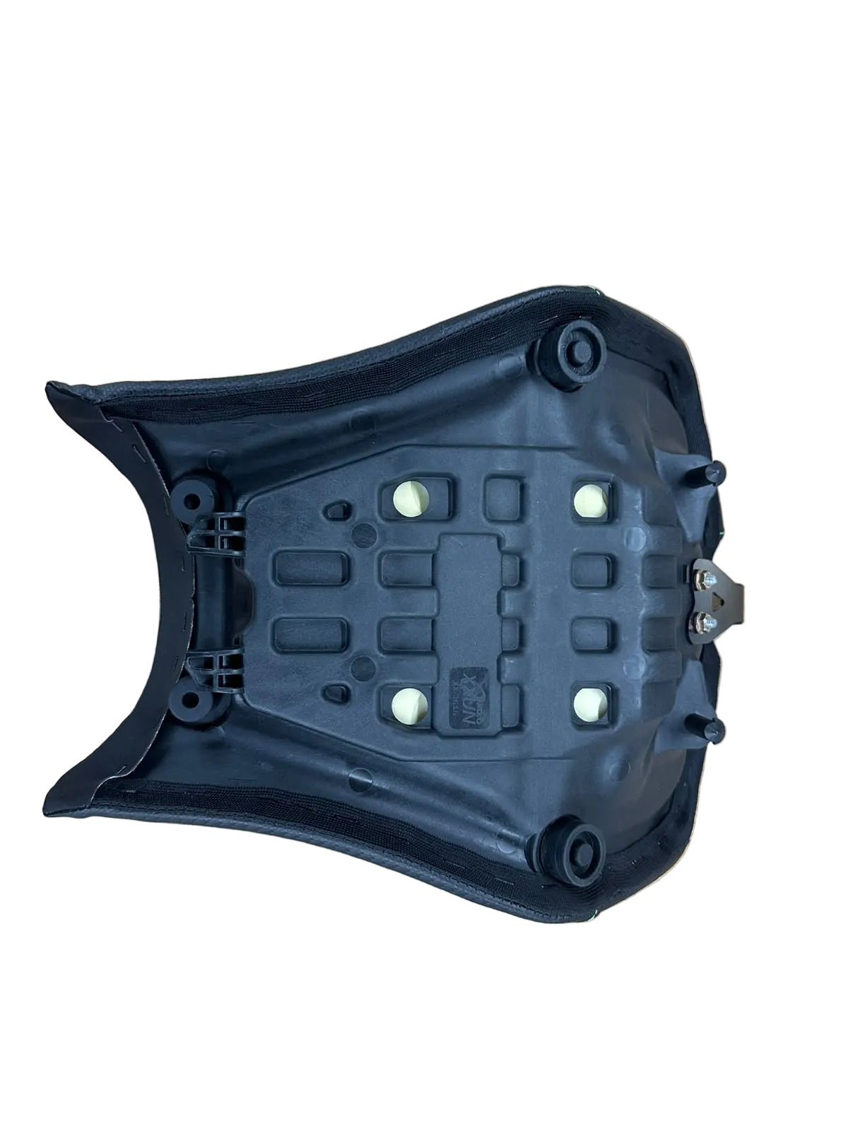 A black molded plastic motorcycle or scooter seat shell, showing the underside with mounting points and small white circular inserts, photographed on a light wood grain surface.