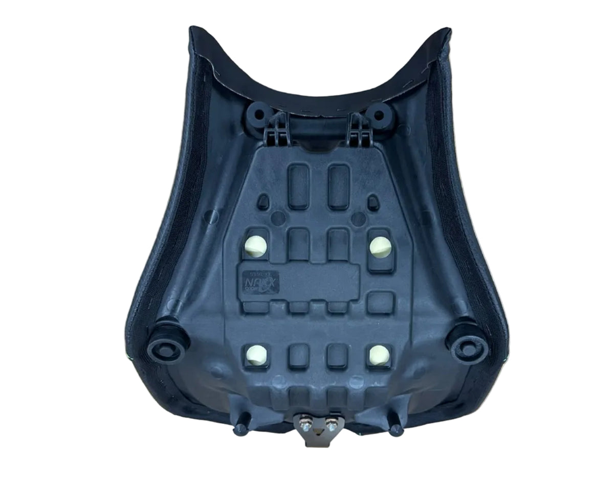 A black molded plastic motorcycle or scooter seat shell, showing the underside with mounting points and small white circular inserts, photographed on a light wood grain surface.